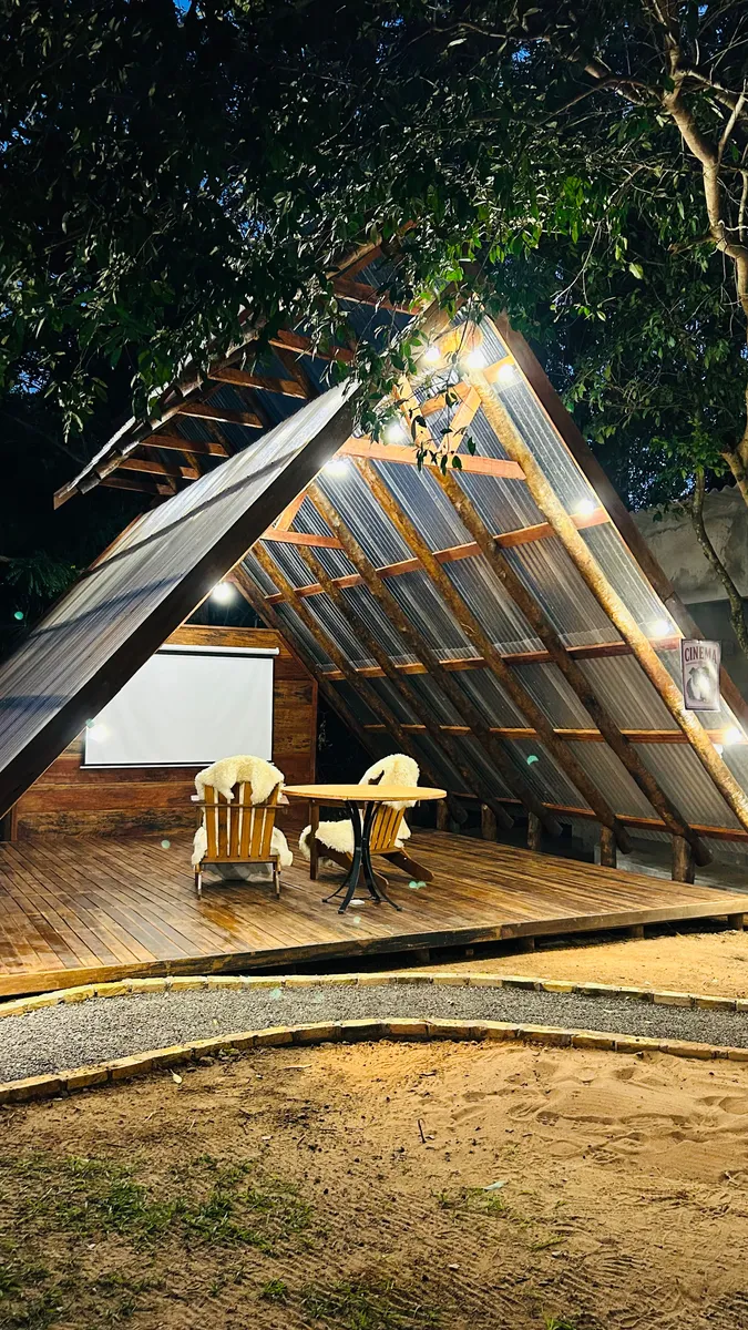 Cinema ao ar livre com telão e poltronas sob a estrutura de madeira